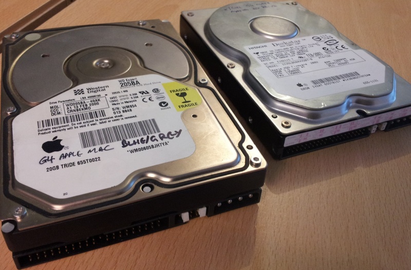 A pair of hard drives, one from an Apple G3, the other from a Mac G4, both with the Apple Logo on their label. One is a Western Digital Expert WD205BA 20GB and the is a 60GB Hitachi Deskstar IC35L060AVV207-0. These drives awaiting file transfer. 