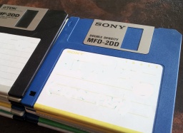 A stack of 3.5 inch floppy disks by Sony, TDK and Verbatim. There are 2 piles of disks with showing their aluminium dust covers and hard plastic protective cases. The disks are photographed side on. 